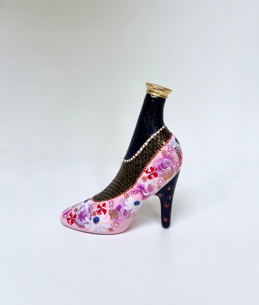 Decoratieve schoen met hoge hak en een roze-zwart bloemenpatroon op een witte achtergrond.