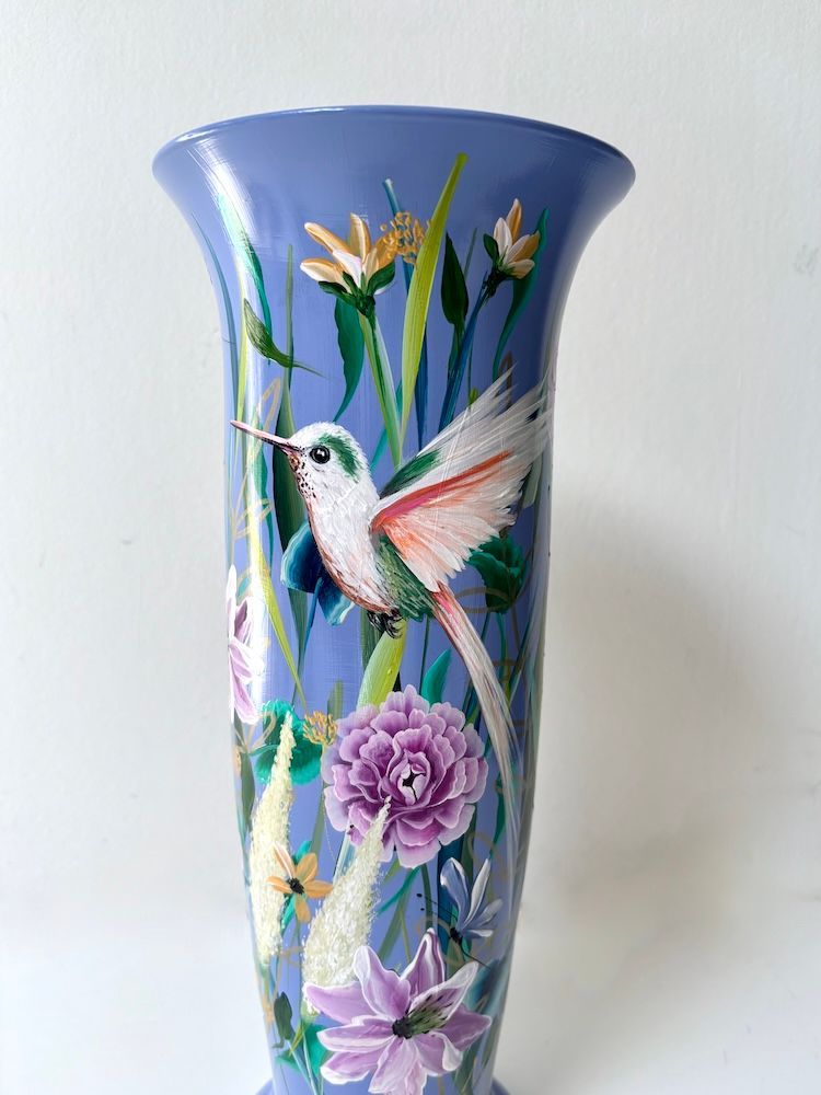 Blauwe keramische vaas met geschilderde kolibrie en roze bloemen.