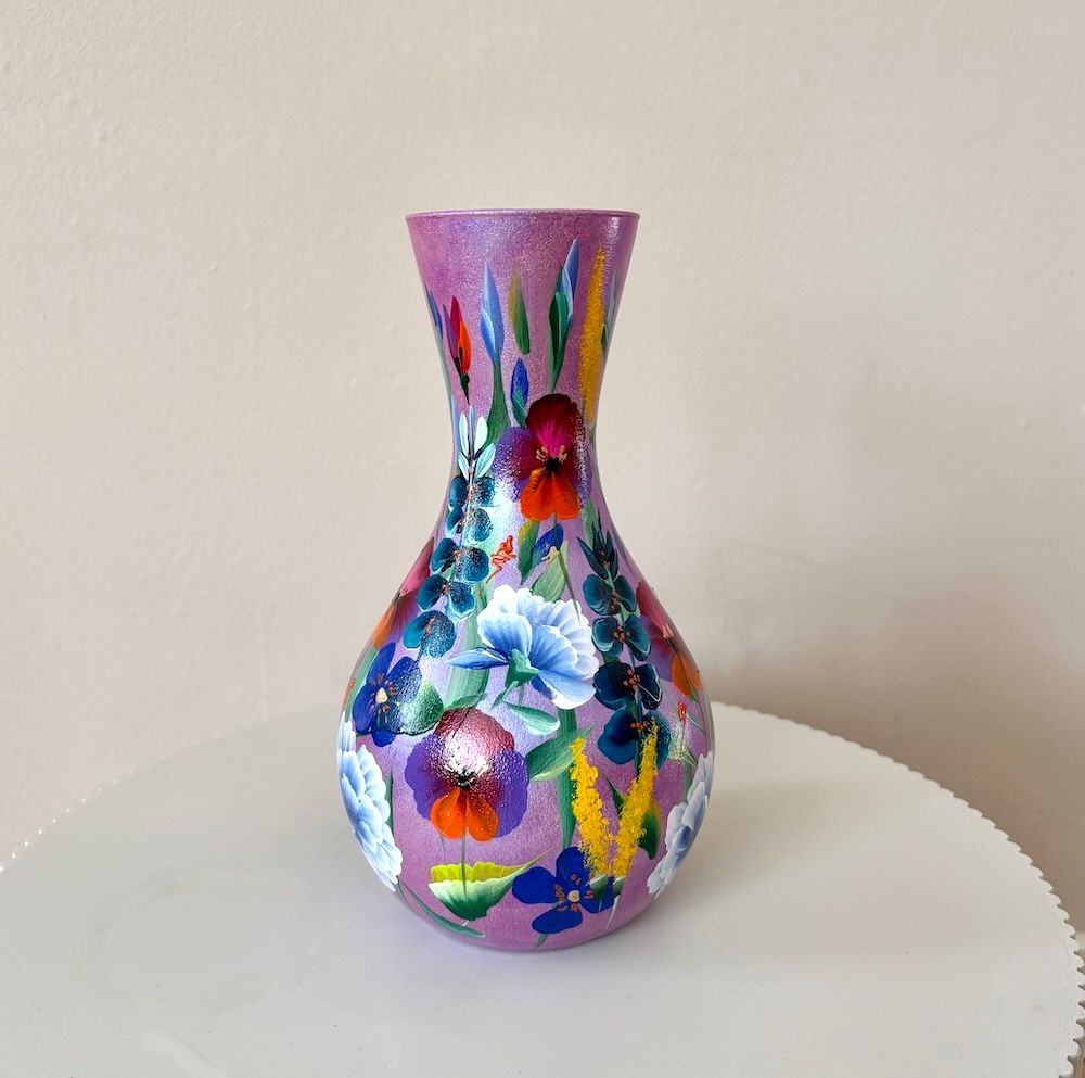 Een handbeschilderde, bolvormige, lavendelkleurige vaas met kleurrijke bloemenpatronen op een neutrale achtergrond.