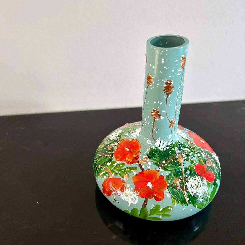 Handbeschilderde turquoise vaas met rode bloemen en groene bladeren op een donkere achtergrond.