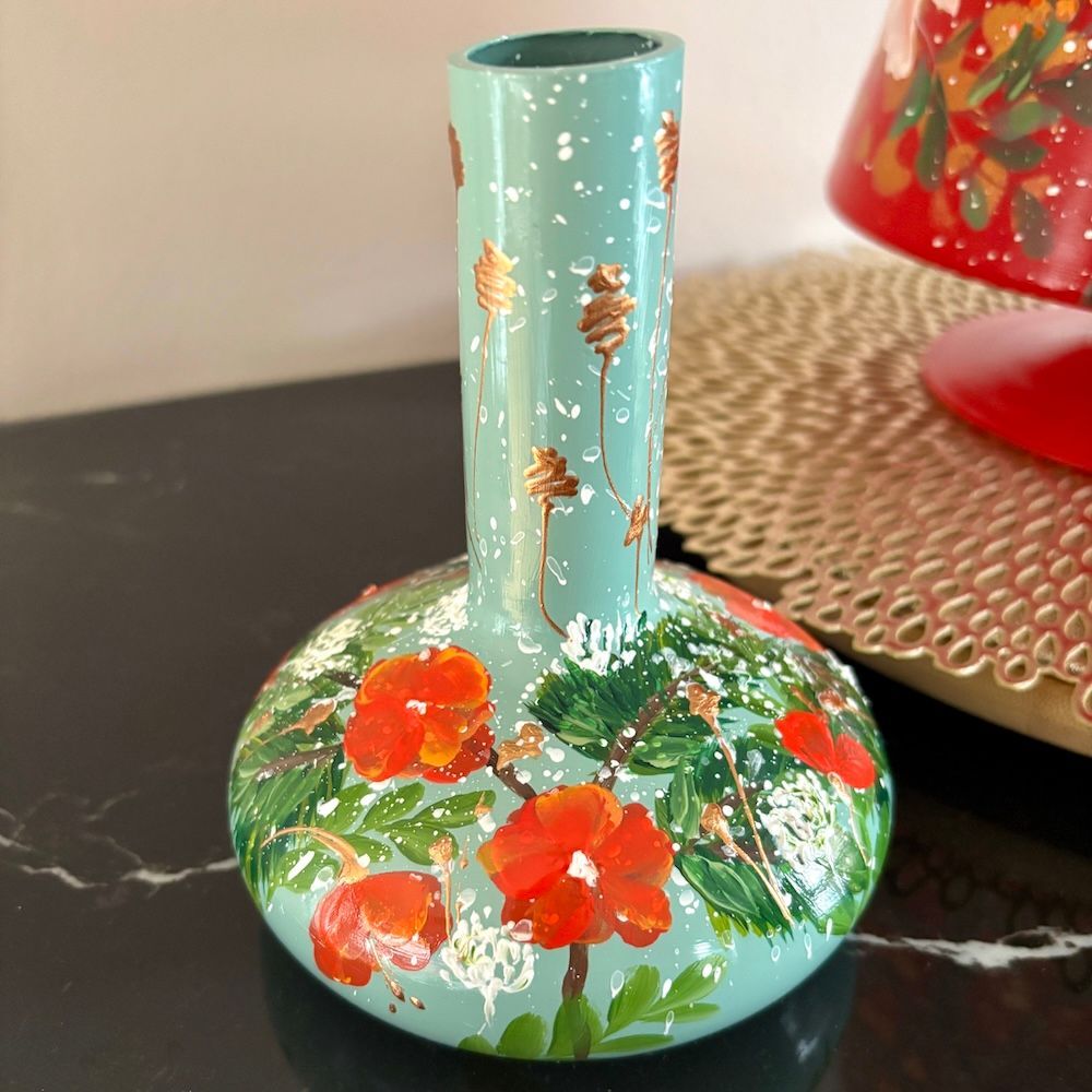 Handbeschilderde turquoise vaas met rode bloemen en groene bladeren op een donkere achtergrond.
