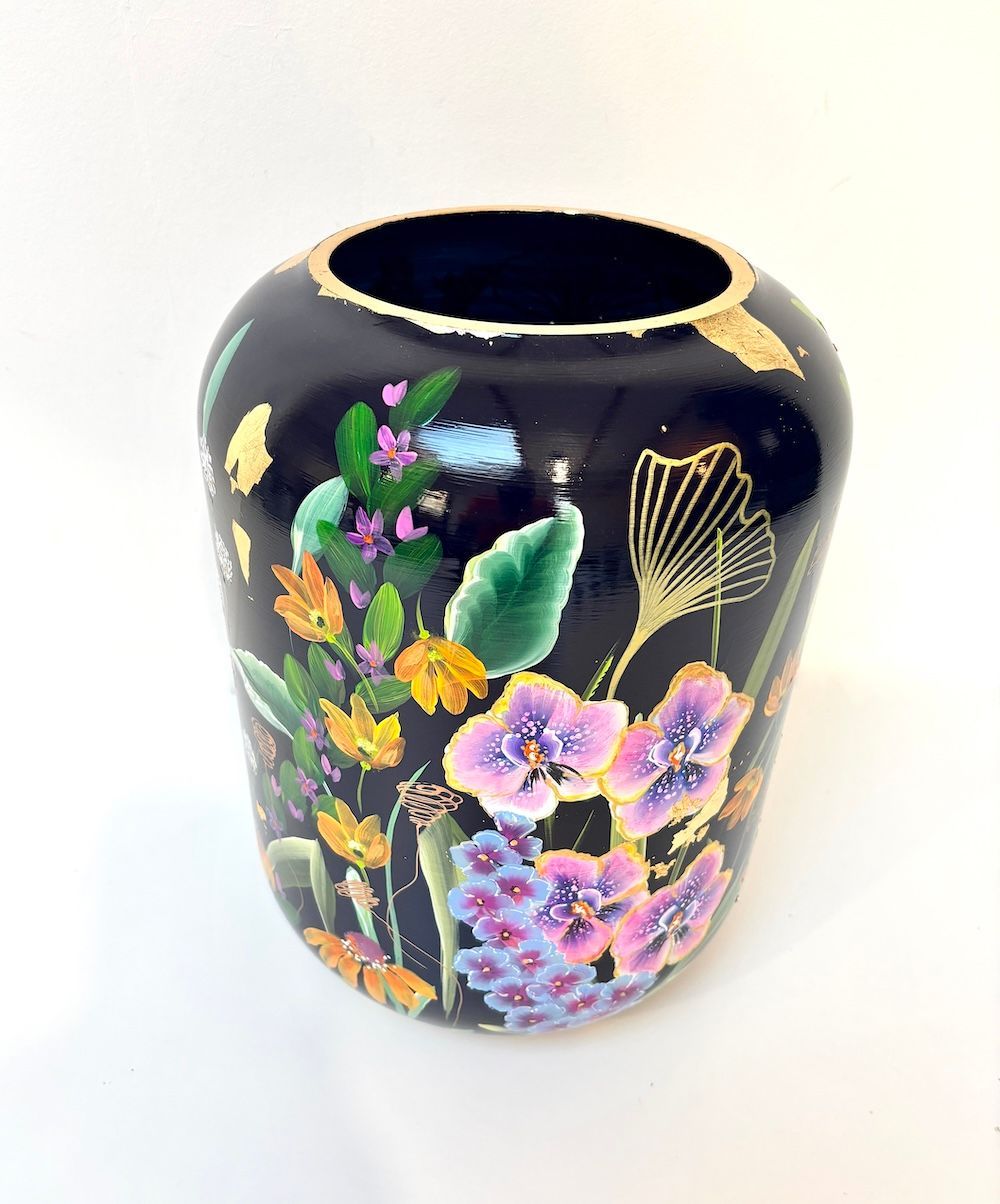 Een zwarte cilindervormige vaas versierd met een kleurrijke ijsvogel, delicate bloemen en bladgoud.