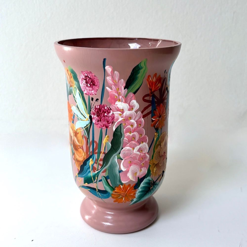 Roze keramische vaas met kleurrijke bloemen- en bladmotieven op een witte achtergrond.