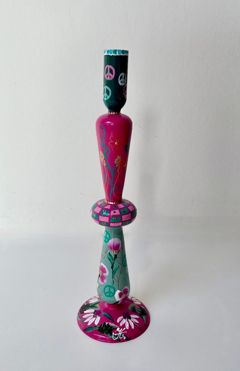 Een handbeschilderde kaarsenhouder met levendige roze en turquoise vlakken, versierd met bloemen, vredessymbolen en patronen.
