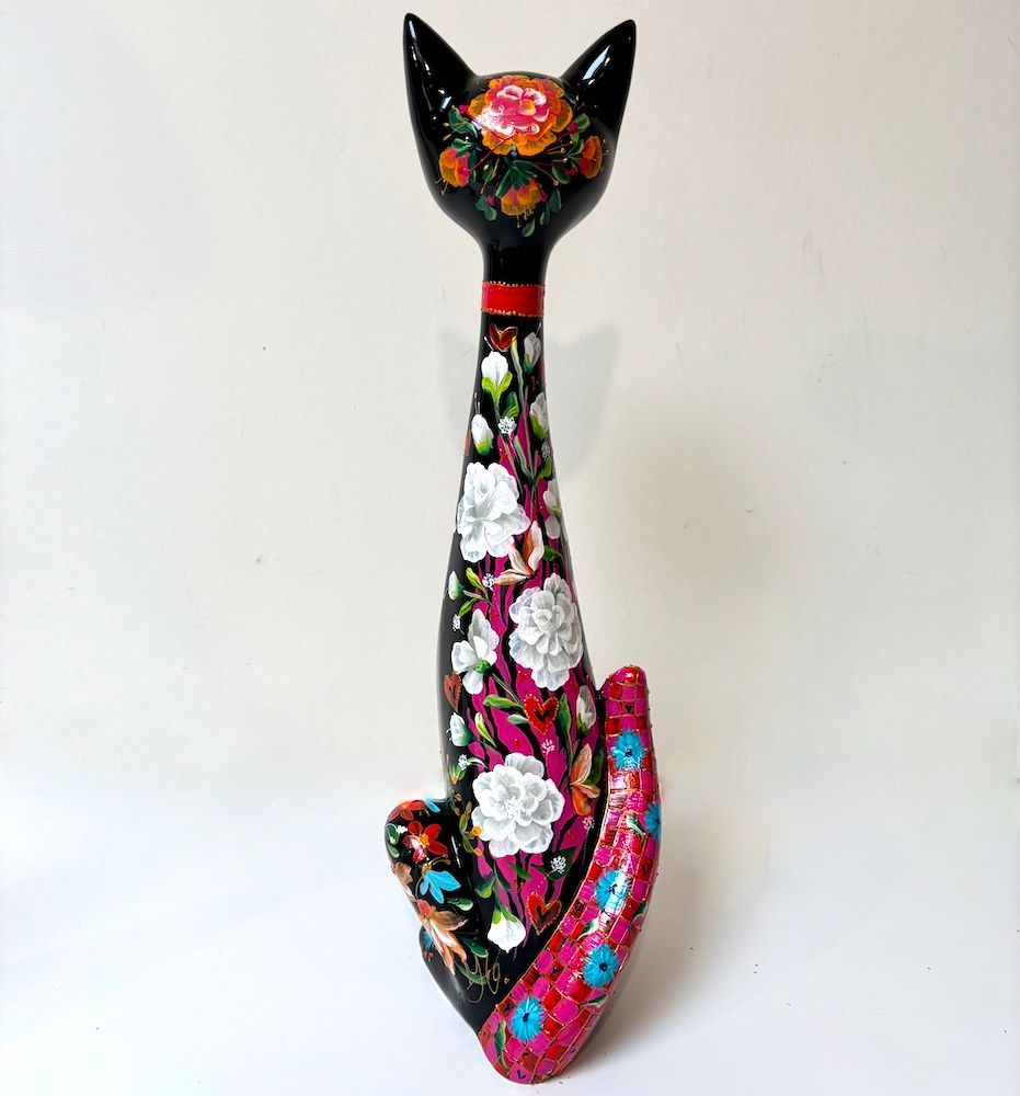 Decoratieve sculptuur van een zwarte kat met kleurrijke bloemmotieven en een lange, gebogen staart op een witte achtergrond.