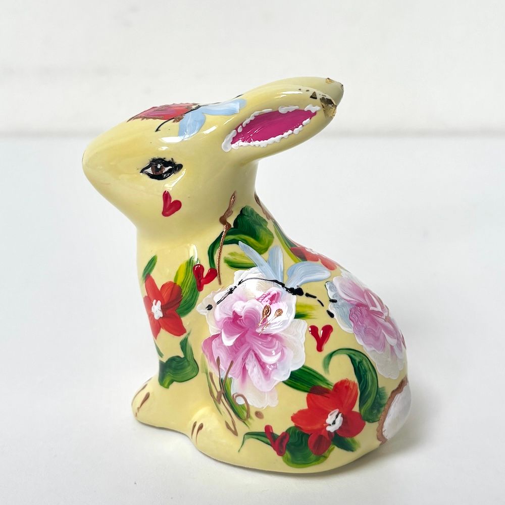 Geel keramisch konijnenbeeldje met bloemen in roze, rode en groene tinten.