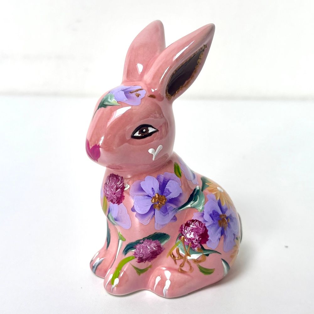 Roze keramisch konijnenbeeldje met paars bloemenpatroon op een witte achtergrond.