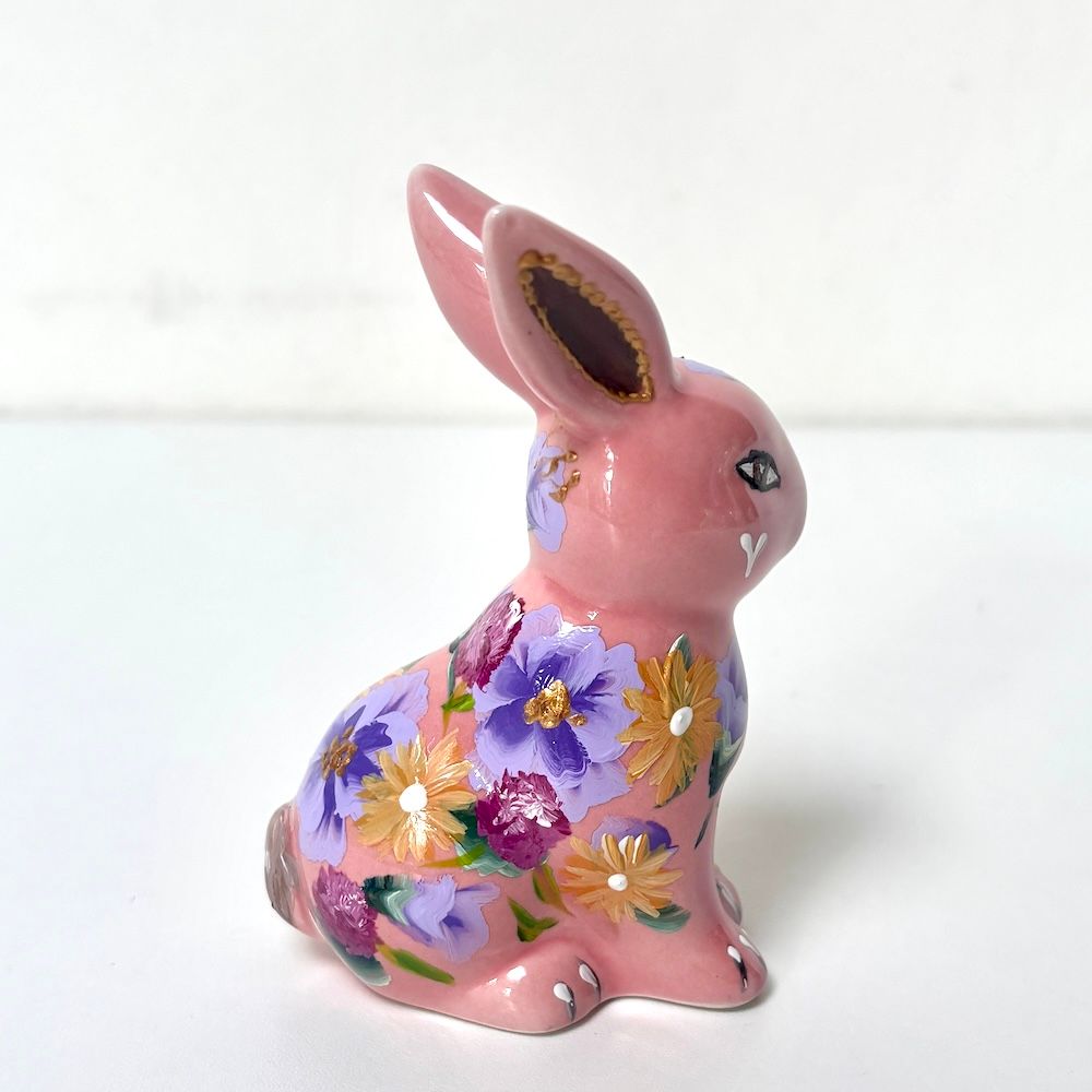 Roze keramisch konijnenbeeldje met paars bloemenpatroon op een witte achtergrond.