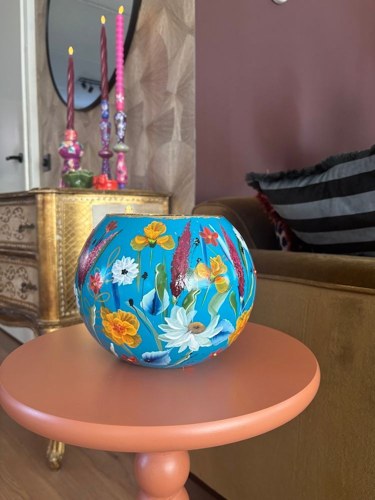 Een ronde, turquoise vaas, beschilderd met levendige, veelkleurige bloemenpatronen en afgewerkt met een goudkleurige rand.