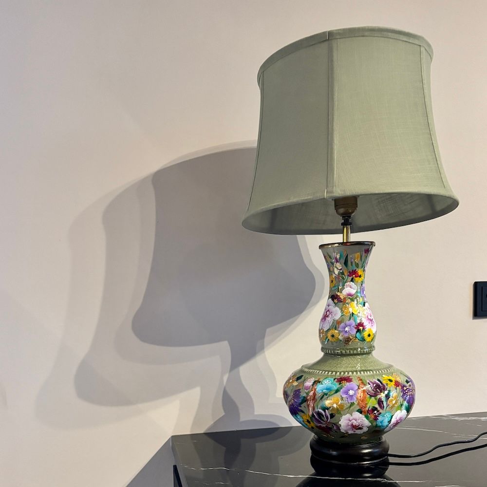 Een decoratieve tafellamp met een bloemvormige keramische voet en een lichtgroene cilindervormige lampenkap,