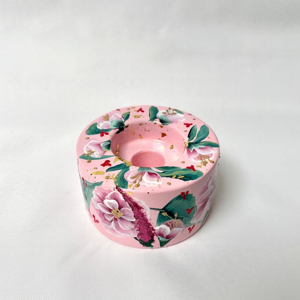 Een lichtroze betonnen kaarsenhouder, handbeschilderd met gedetailleerde roze bloemen, groene bladeren en gouden accenten.