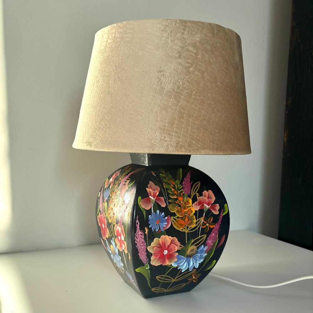 Tafellamp met geschilderd bloemenmotief en beige kap op een witte ondergrond.