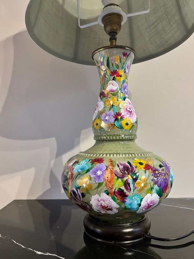 Een handbeschilderde lamp met een gestructureerde, lichtgroene voet, met kleurrijke bloemen, op een lampen standaard.
