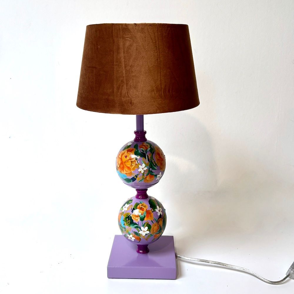Kleurrijk beschilderde lamp met groene kap en paarse voet op een witte ondergrond.