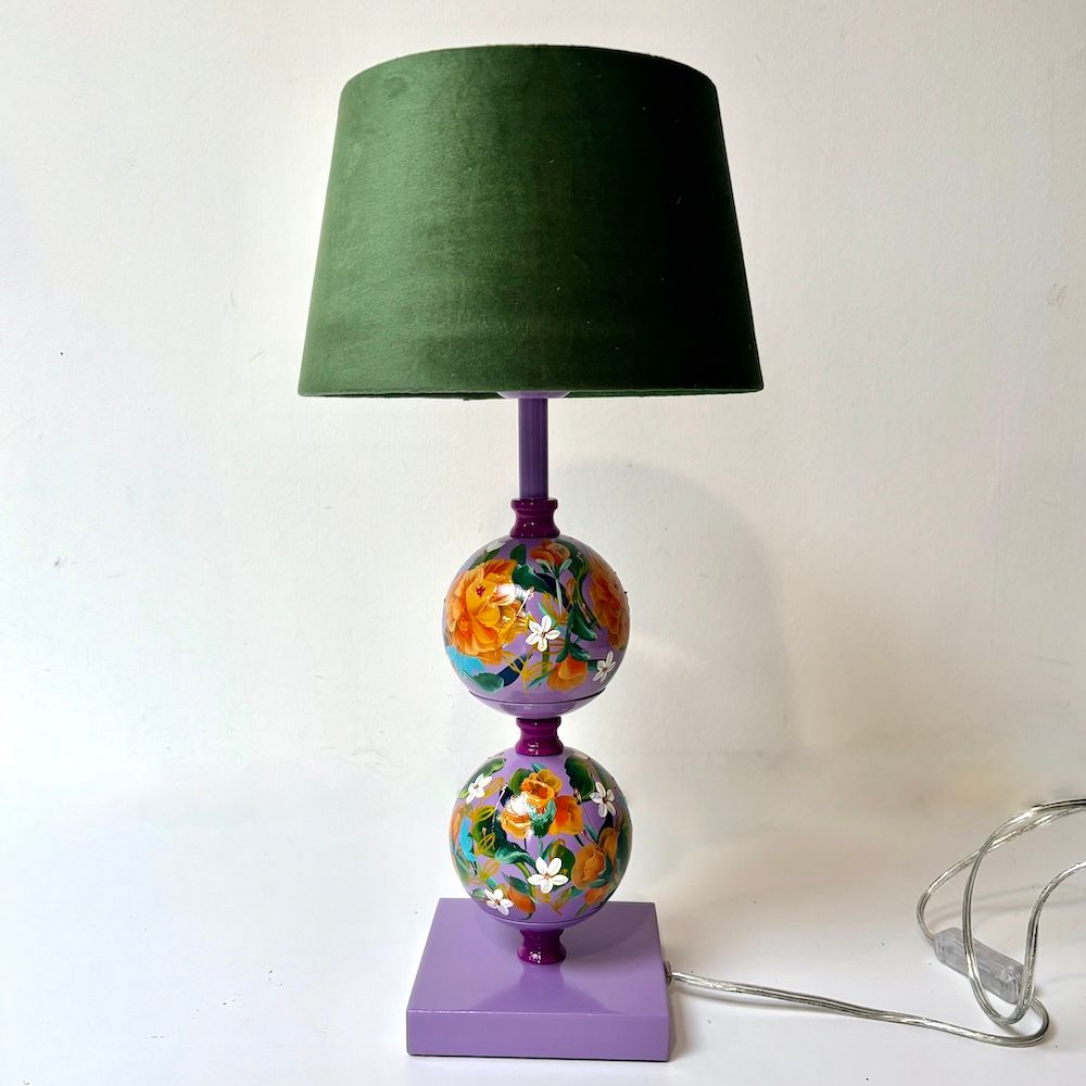 Kleurrijk beschilderde lamp met groene kap en paarse voet op een witte ondergrond.