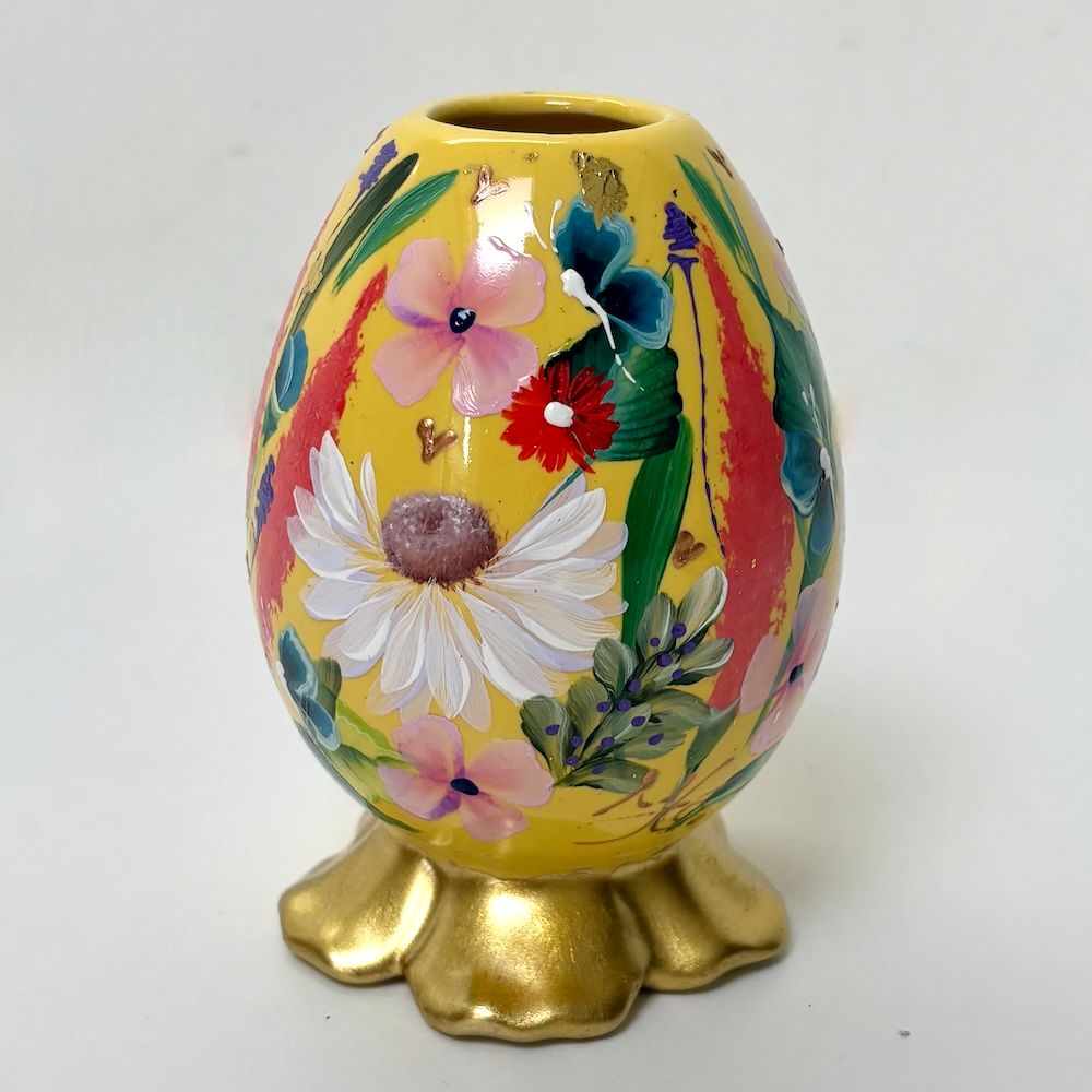 Decoratieve gele eivormige vaas met handgeschilderde roze en witte bloemen op een gouden voet.
