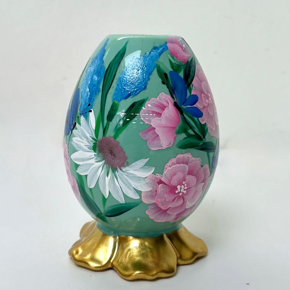 Versierd pastelkleurig ei met bloemenmotief op een gouden standaard