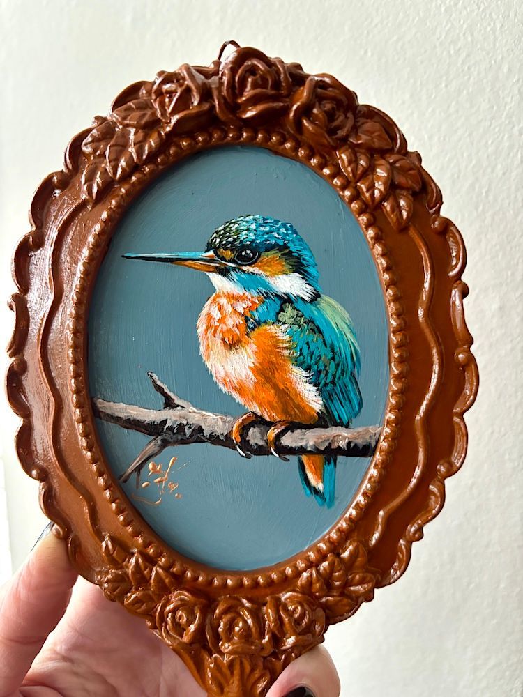 Decoratieve ovale handspiegel met een geschilderde vogel in een blauw midden en een sierlijke bruine lijst.