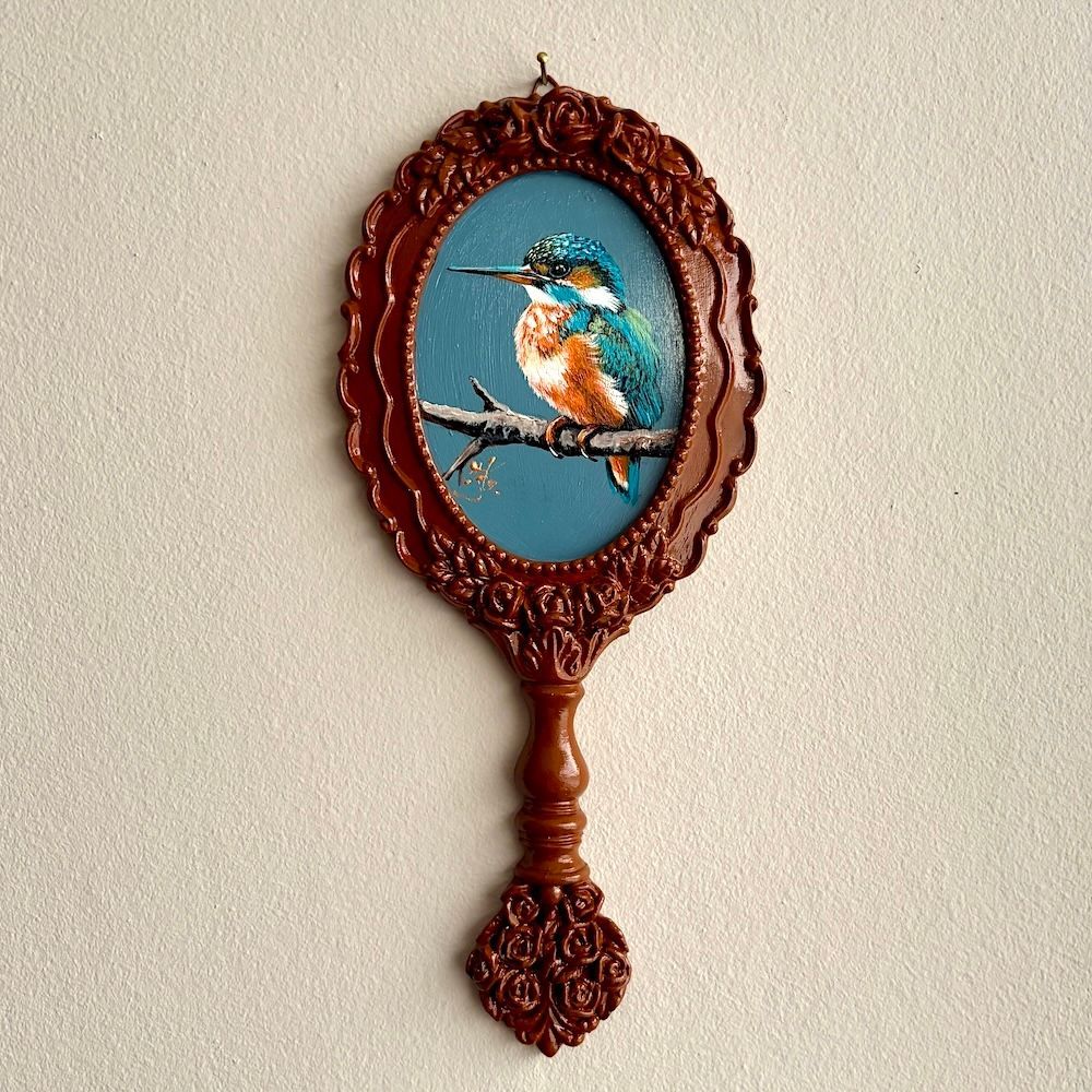 Decoratieve ovale handspiegel met een geschilderde vogel in een blauw midden en een sierlijke bruine lijst.
