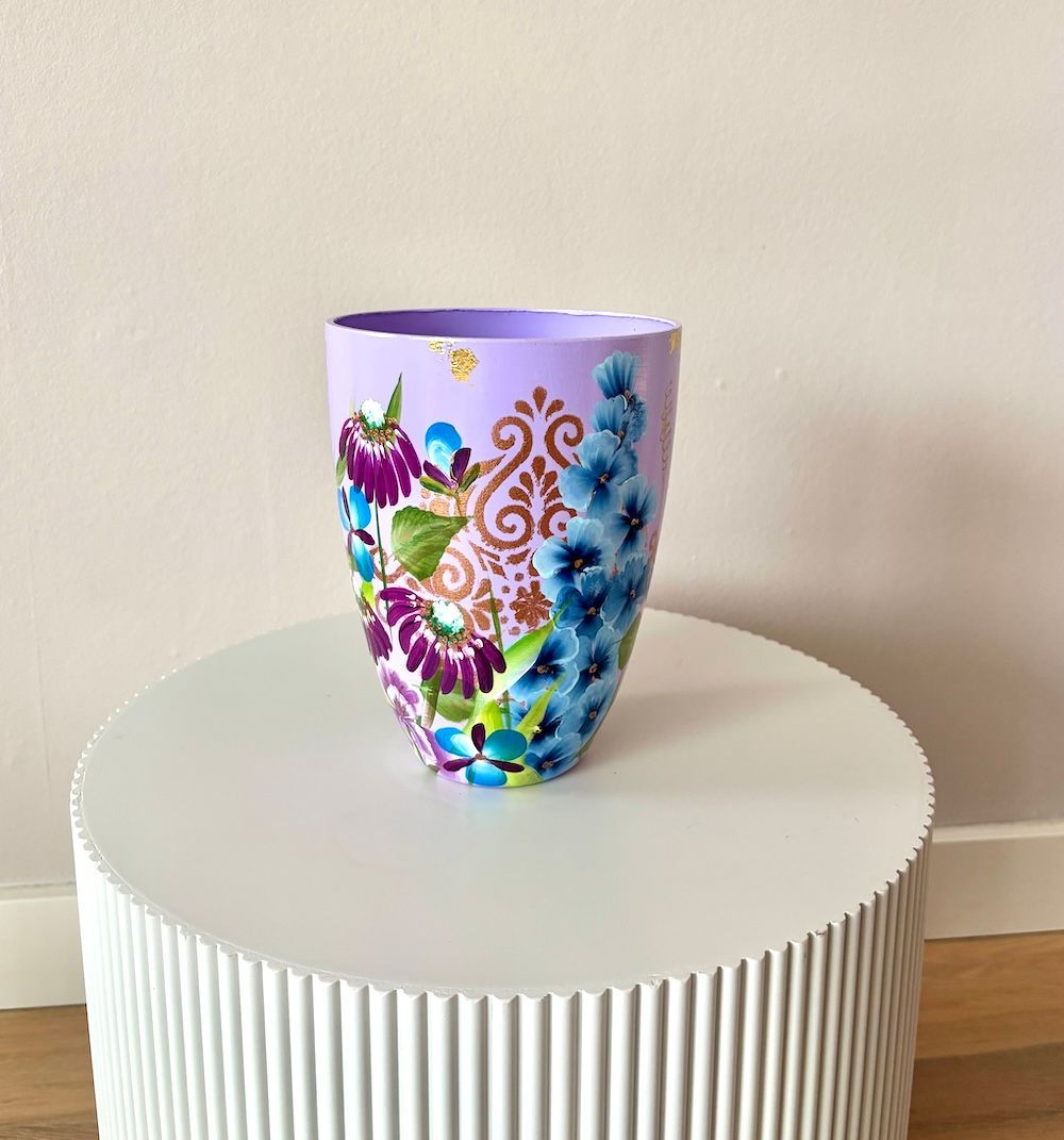 Een lavendelvaas versierd met kleurrijke paarse, blauwe en gouden bloemmotieven, staat op een witte, ronde tafel