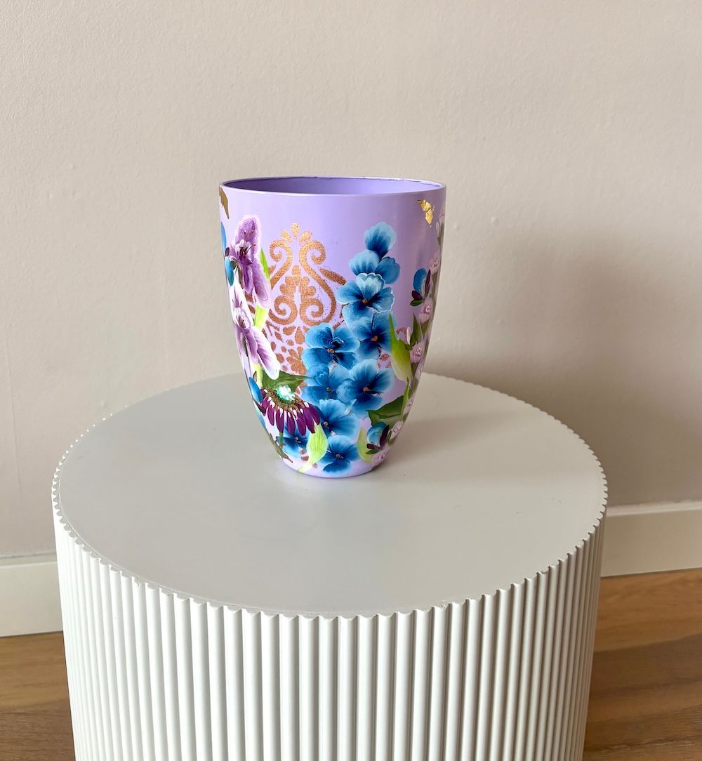 Een lavendelvaas versierd met kleurrijke paarse, blauwe en gouden bloemmotieven, staat op een witte, ronde tafel