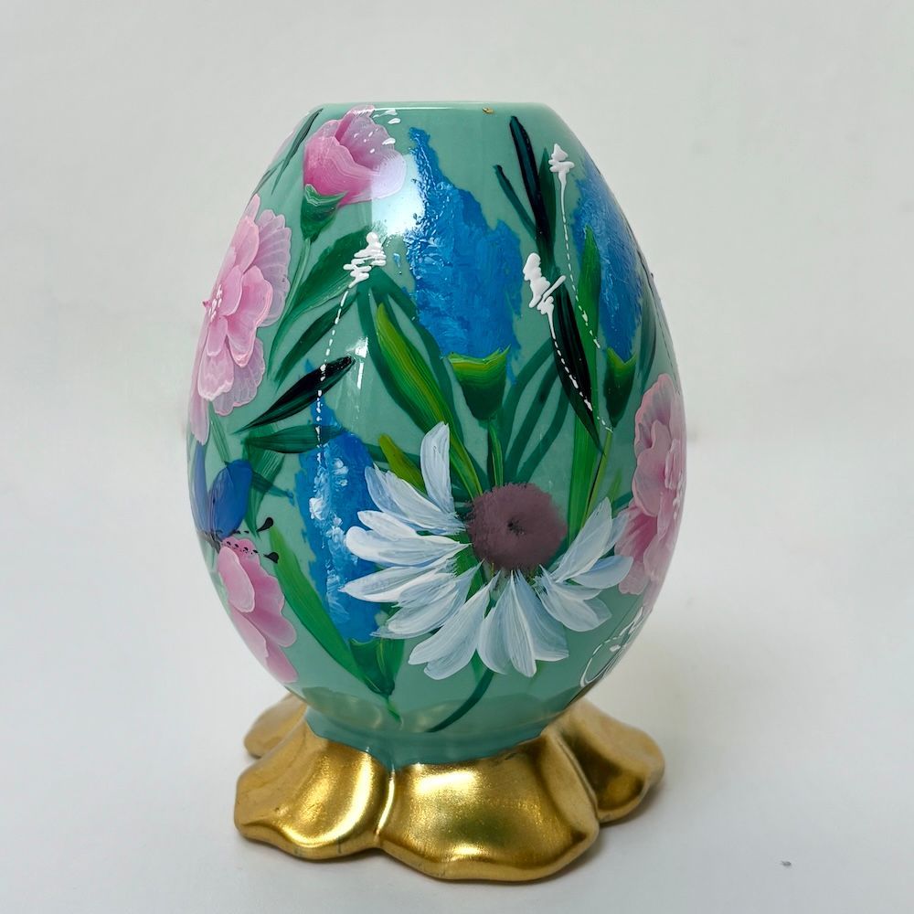 Versierd pastelkleurig ei met bloemenmotief op een gouden standaard