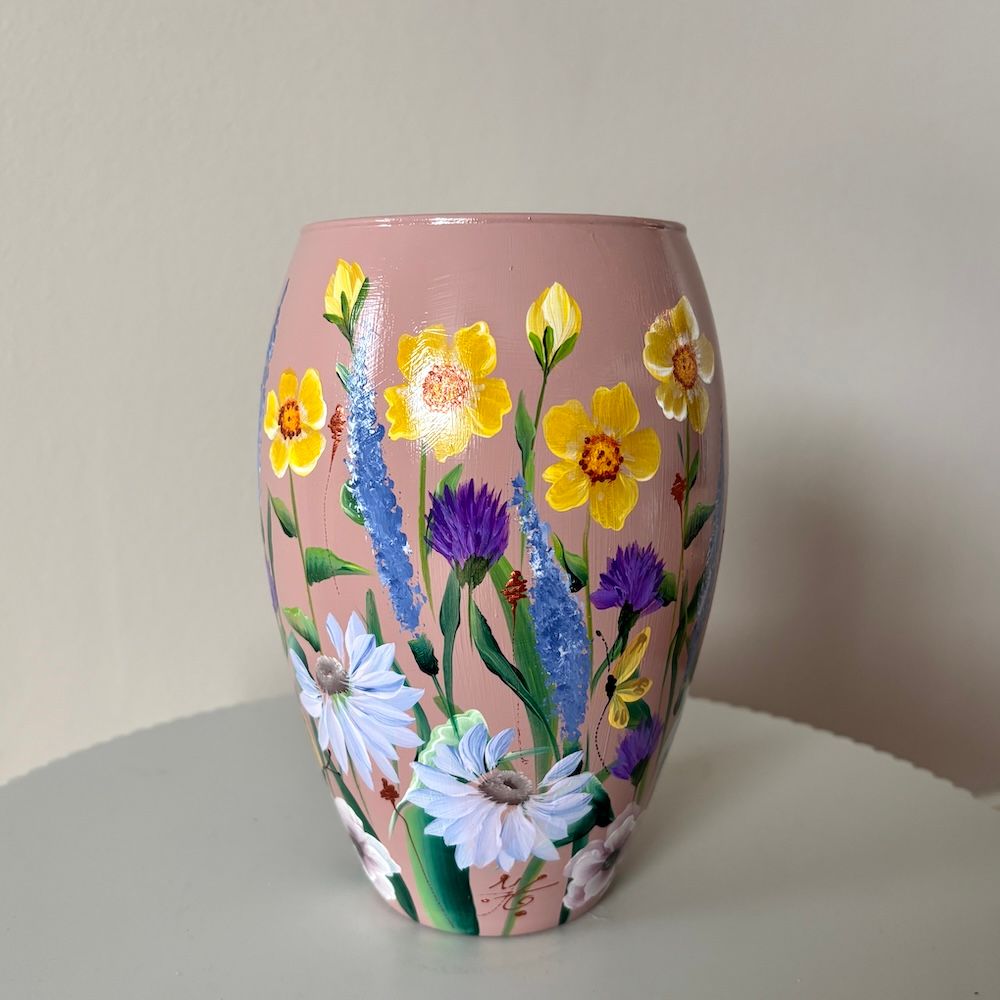 Een vaas met een mauve achtergrond, beschilderd met een levendig boeket gele, paarse en witte wilde bloemen.