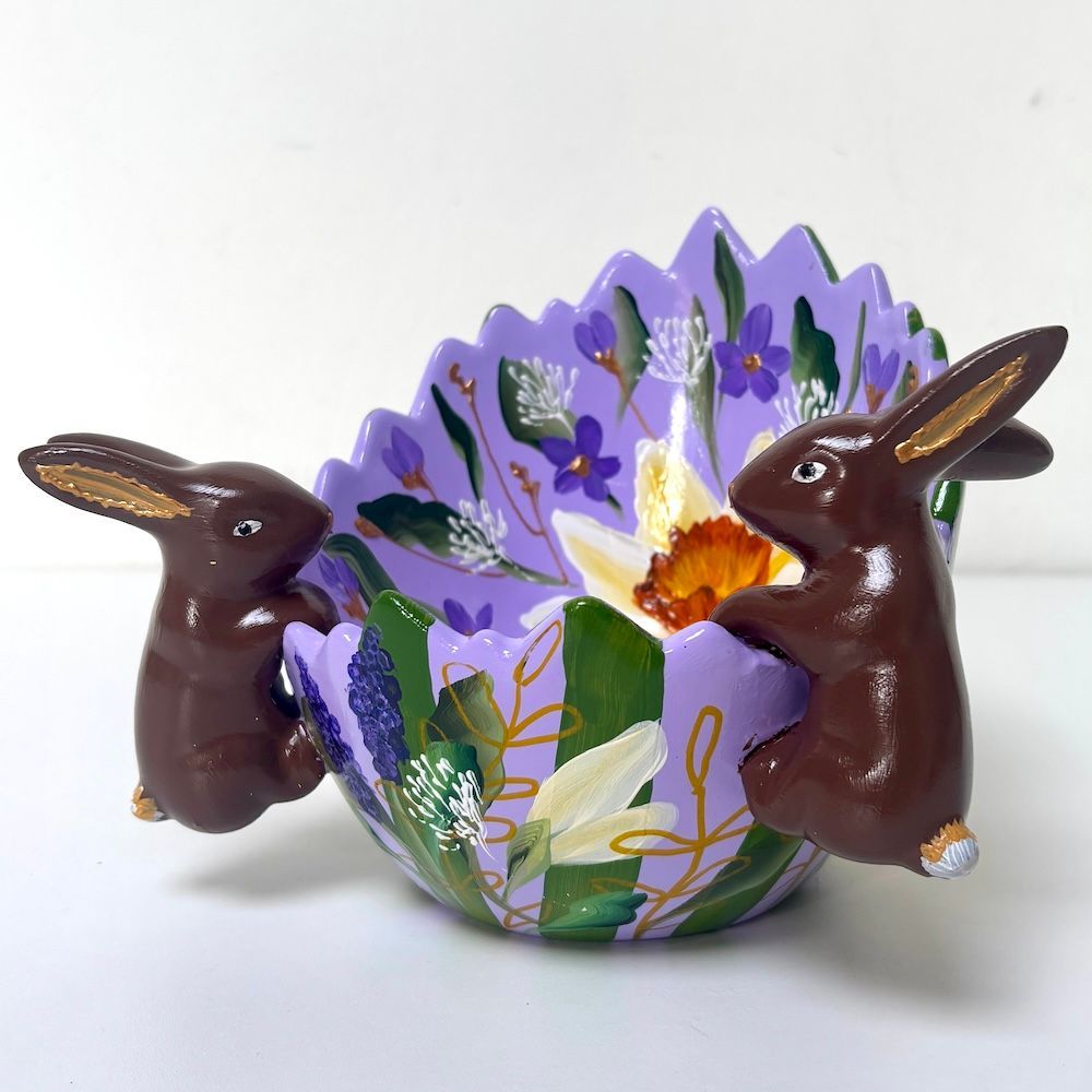Twee chocoladekonijntjes naast een paarse paasmand met bloemen.