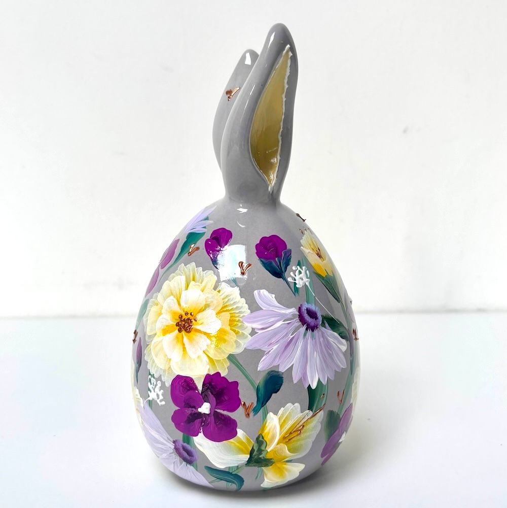 Grijze keramische konijnenfiguur met handgeschilderde bloemmotieven in geel, paars en groen.