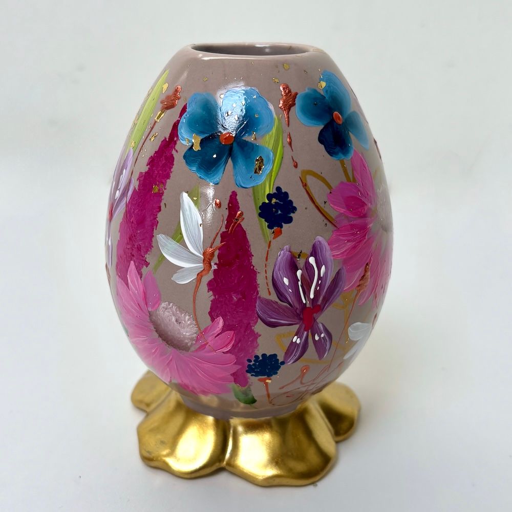Versierd roze eivormig ornament met kleurrijke bloemmotieven op een gouden standaard