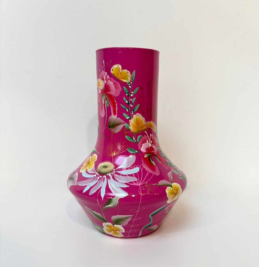 Een magentakleurige vaas met een brede voet en een smalle hals, versierd met geschilderde witte roze en gele bloemen.