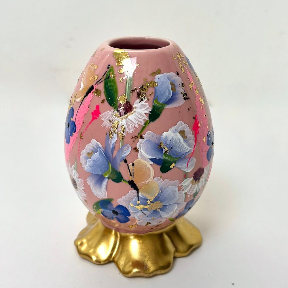 Een eivormige roze vaas met handgeschilderde lichtblauwe bloemen en accenten van bladgoud
