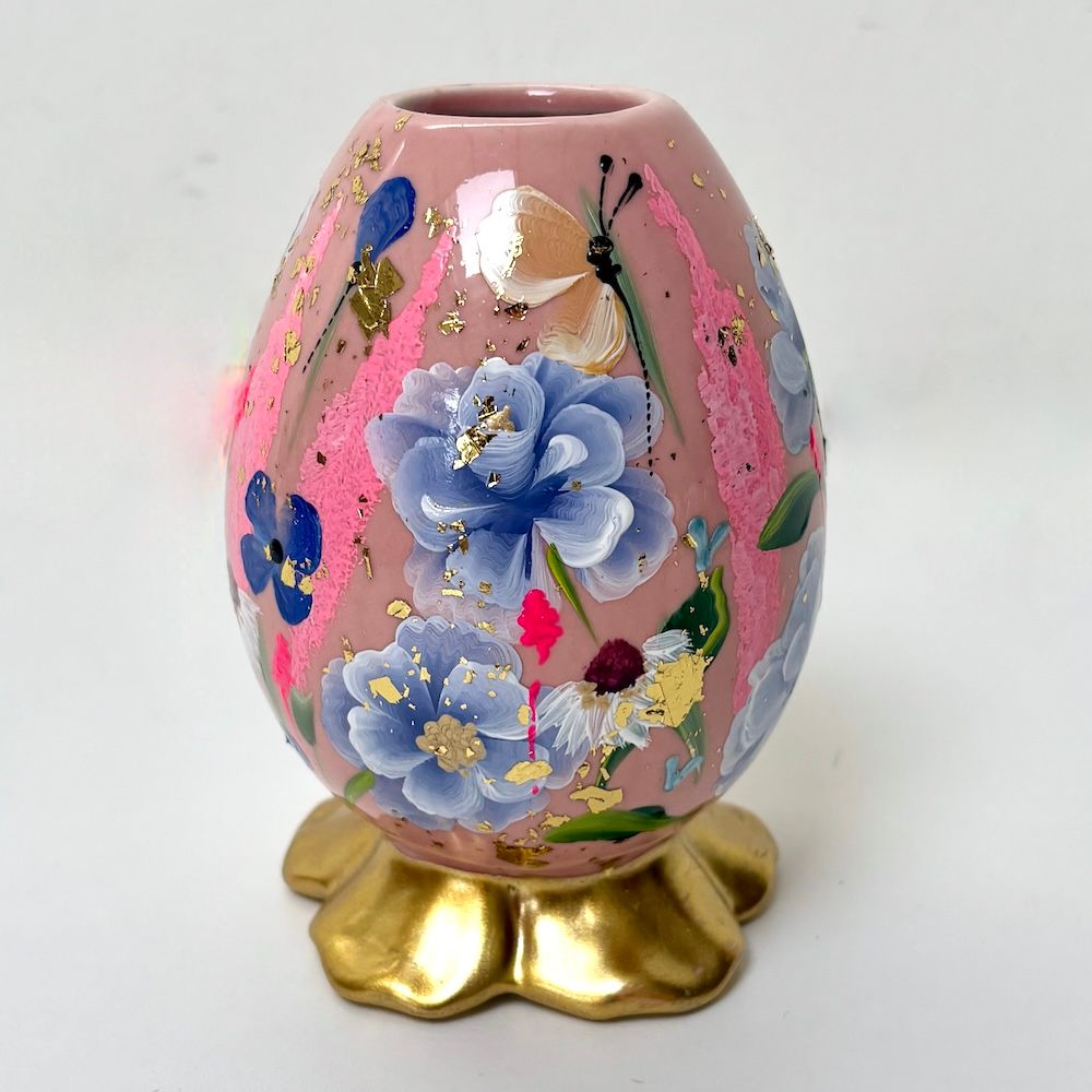 Een eivormige roze vaas met handgeschilderde lichtblauwe bloemen en accenten van bladgoud