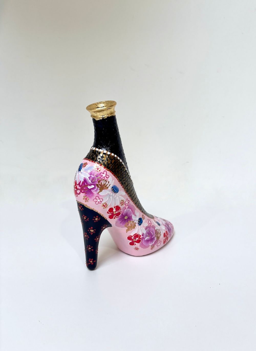 Decoratieve schoen met hoge hak en een roze-zwart bloemenpatroon op een witte achtergrond.