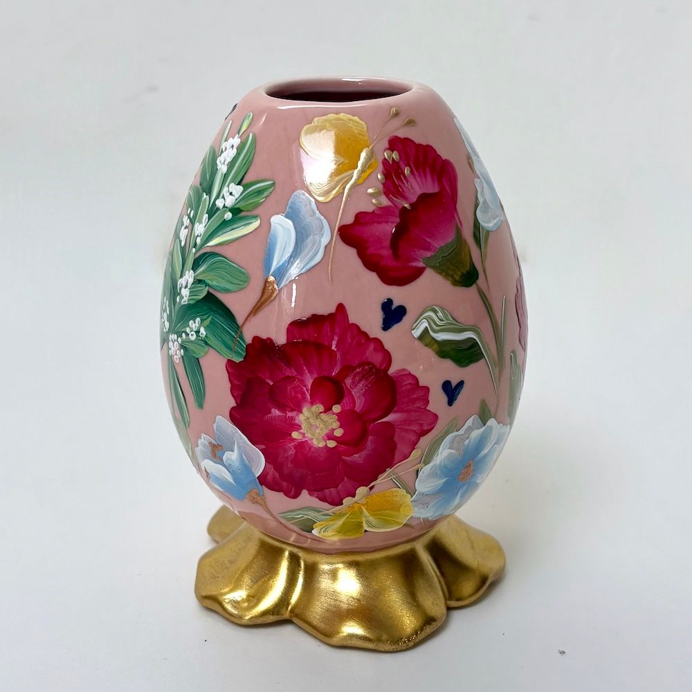 Handbeschilderd bloemenei op een gouden standaard, roze met rode, blauwe, witte en groene bloemen.
