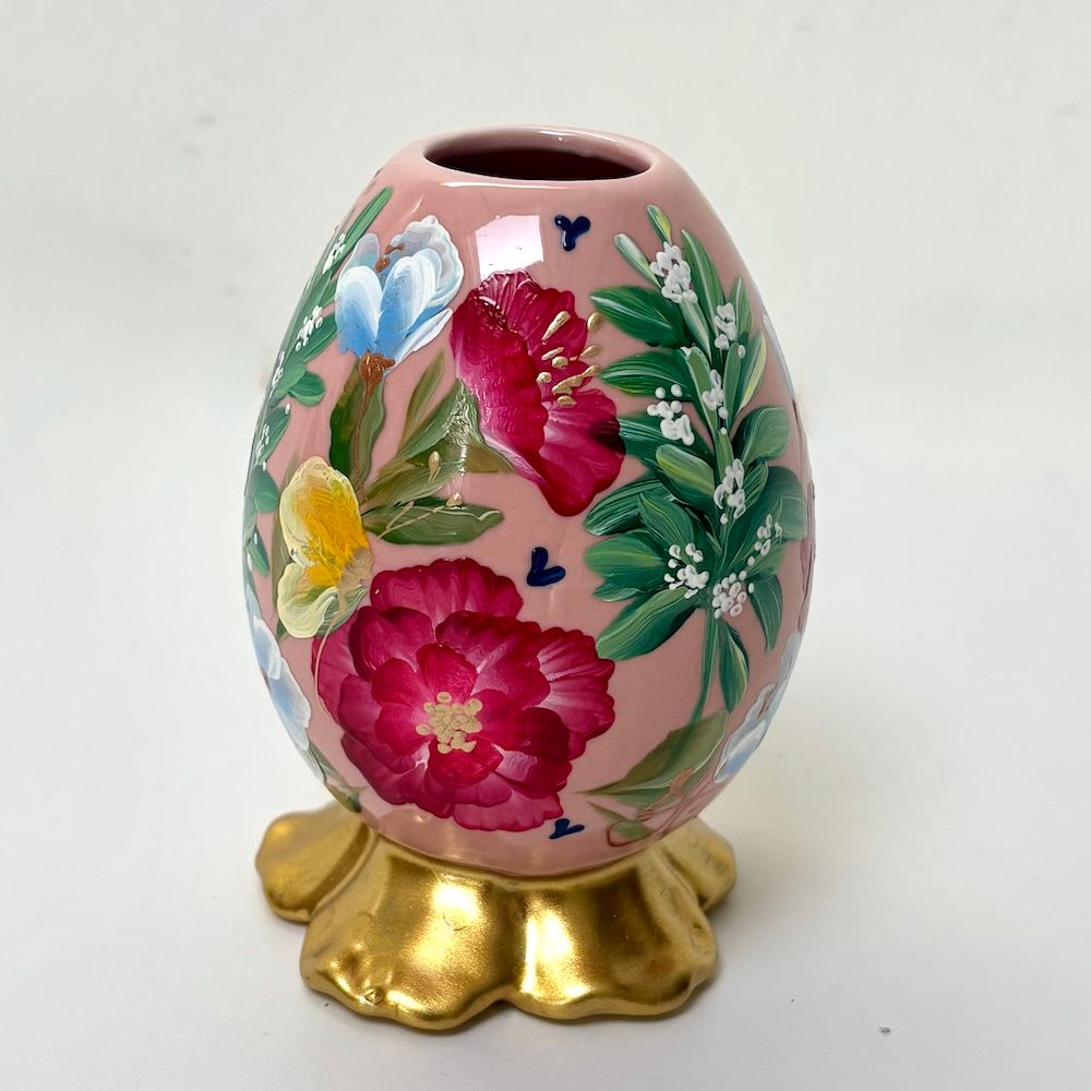 Handbeschilderd bloemenei op een gouden standaard, roze met rode, blauwe, witte en groene bloemen.