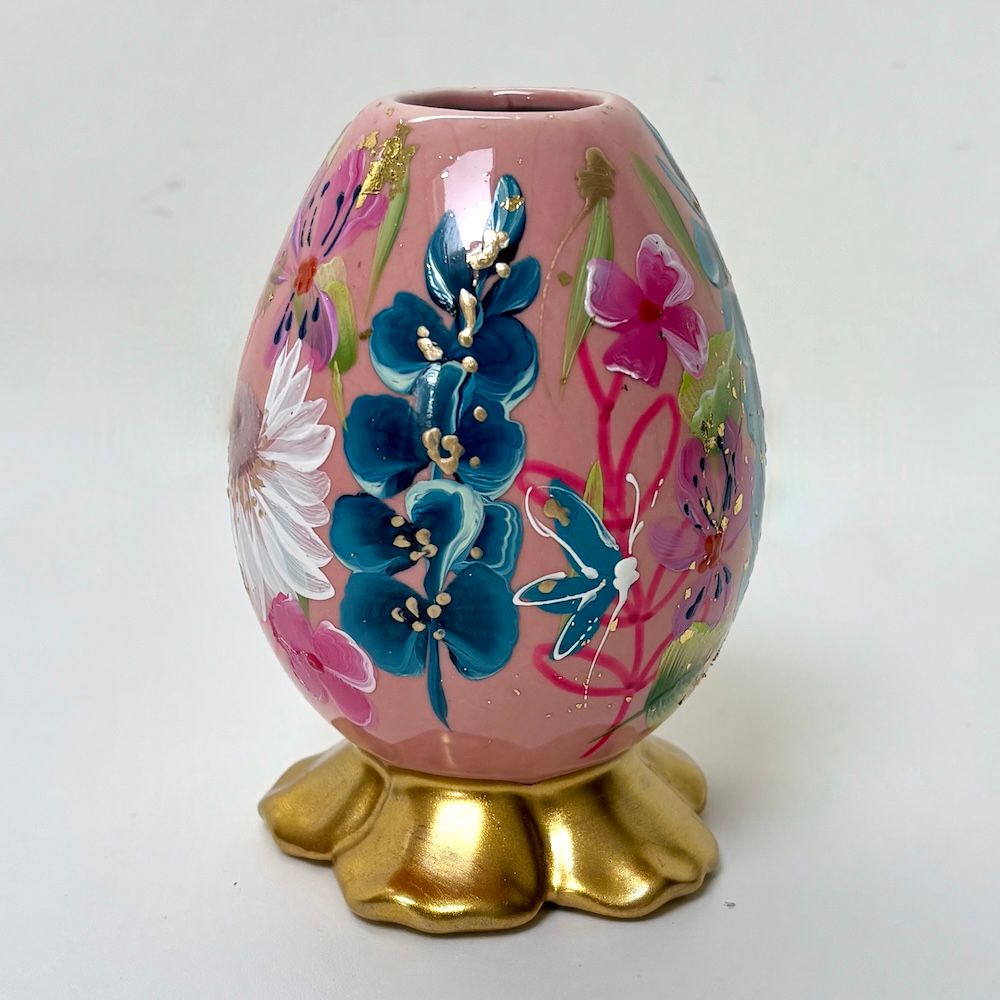 Roze, bloemrijk, eivormig decoratief object op een gouden voetstuk.