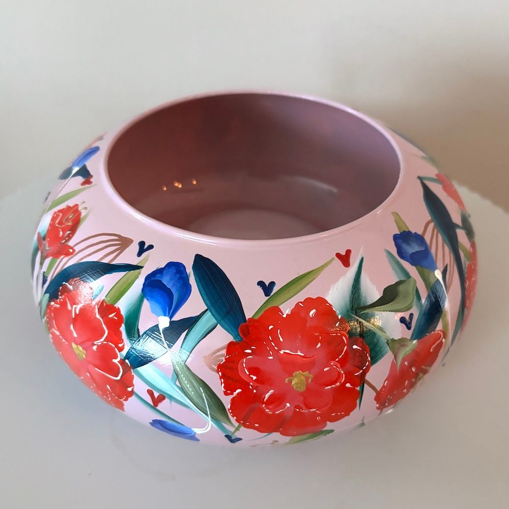 Roze keramische schaal met bloemenmotief op een witte geribbelde voet tegen een effen achtergrond.