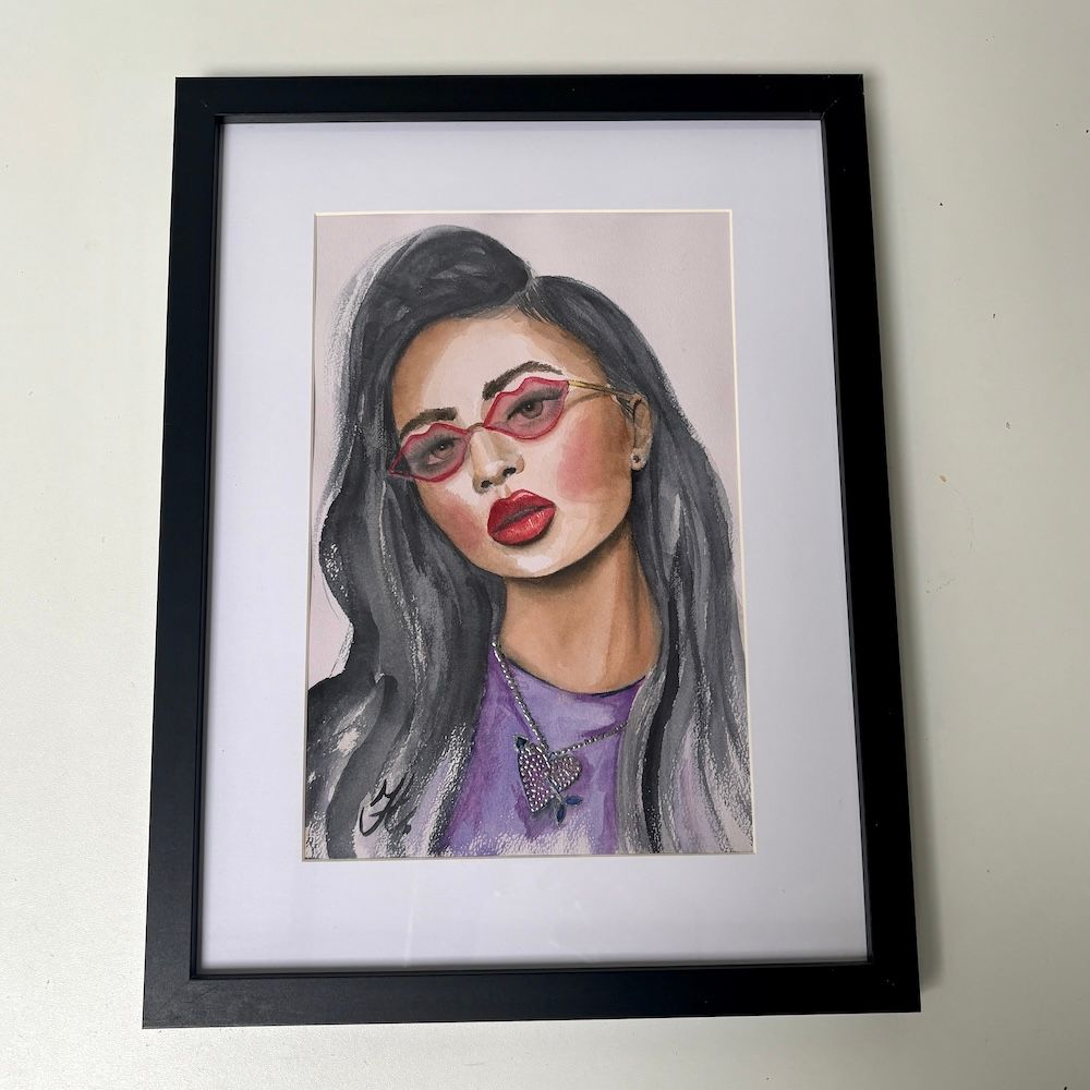 Ingelijste portrettekening van een vrouw met een rode bril, lang donker haar en een paarse top op een witte muur.