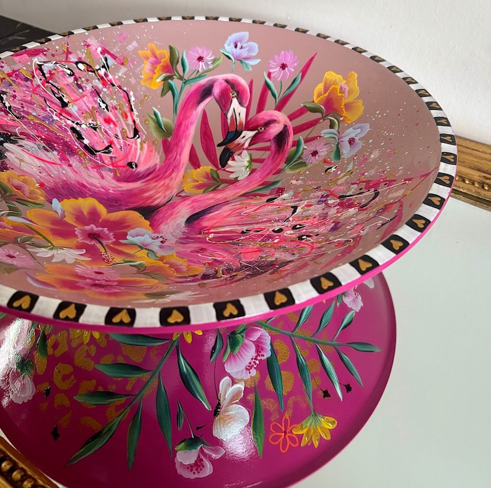 Decoratieve glazen schaal in de vorm van een roze flamingo met bloemen- en tropische patronen op een bijpassende standaard.