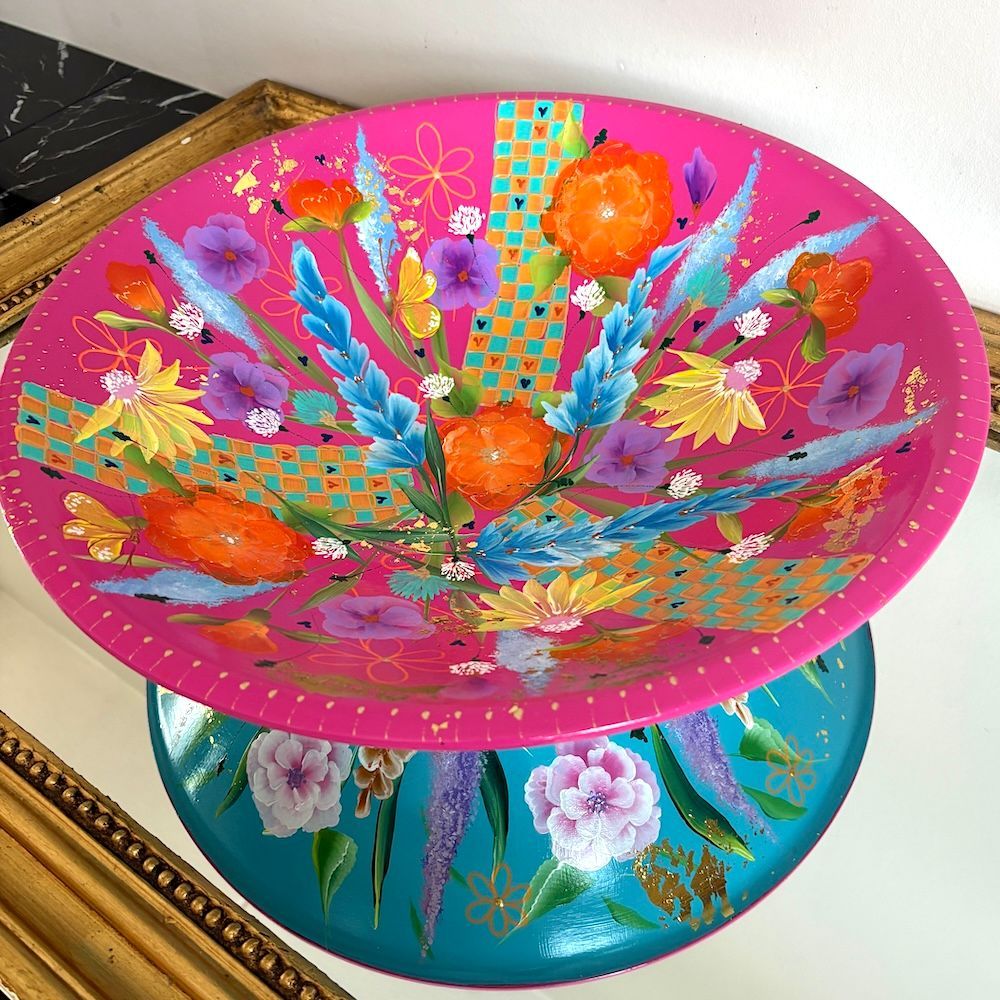 Twee kleurrijke, gedecoreerde kommen op elkaar gestapeld, roze op turquoise met bloemen- en abstracte patronen.