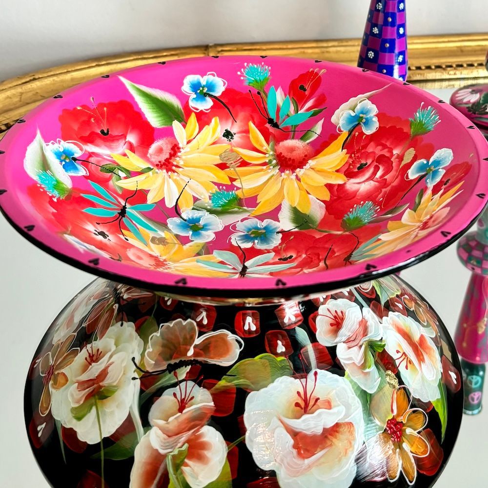 Een rond, felroze decoratief dienblad, beschilderd met een levendig bloemstuk met rode, gele en blauwe bloemen.