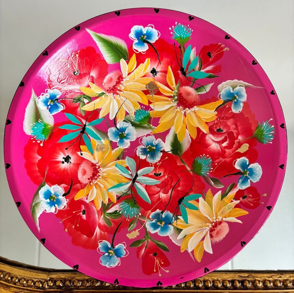 Een rond, felroze decoratief dienblad, beschilderd met een levendig bloemstuk met rode, gele en blauwe bloemen.