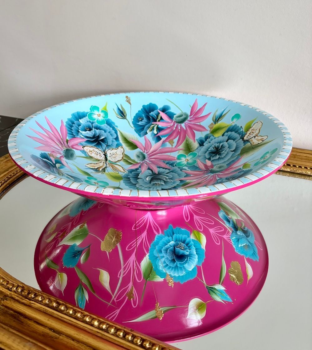 Een schaal met een lichtblauwe binnenkant versierd met bloemmotieven, geplaatst op een spiegel reflecteert de onderkant