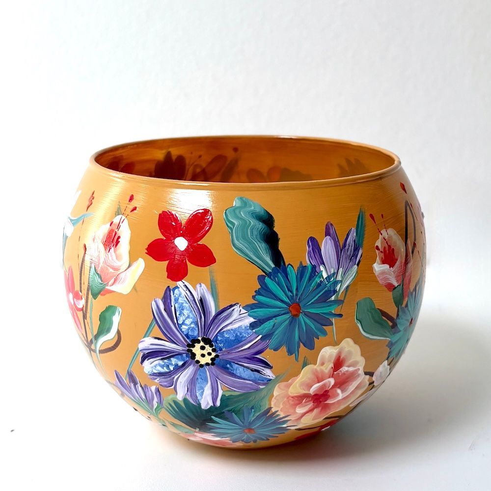 Handbeschilderde oranje kom met kleurrijke bloemmotieven op een witte achtergrond.