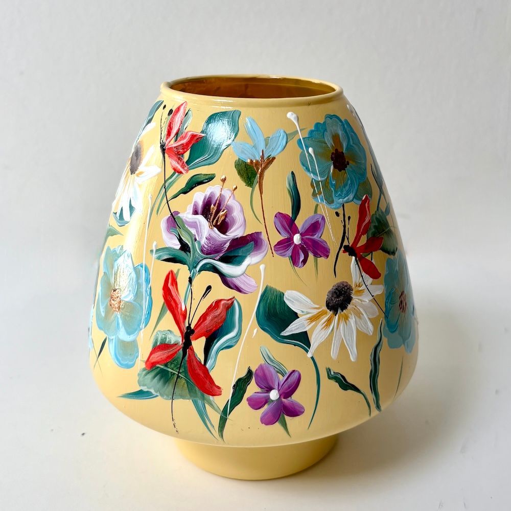 Gele keramische vaas met bloemenmotief, versierd met kleurrijke, beschilderde bloemen op een witte achtergrond.