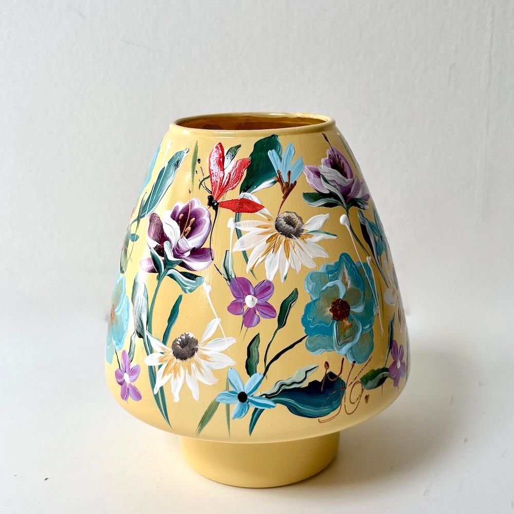 Gele keramische vaas met bloemenmotief, versierd met kleurrijke, beschilderde bloemen op een witte achtergrond.