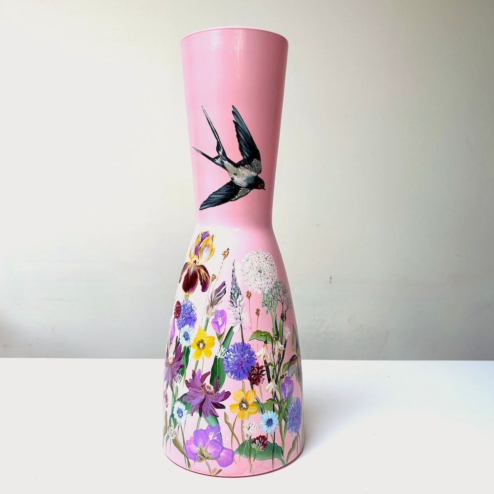 Roze vaas met geschilderde kolibrie en kleurrijke bloemen op een effen achtergrond.