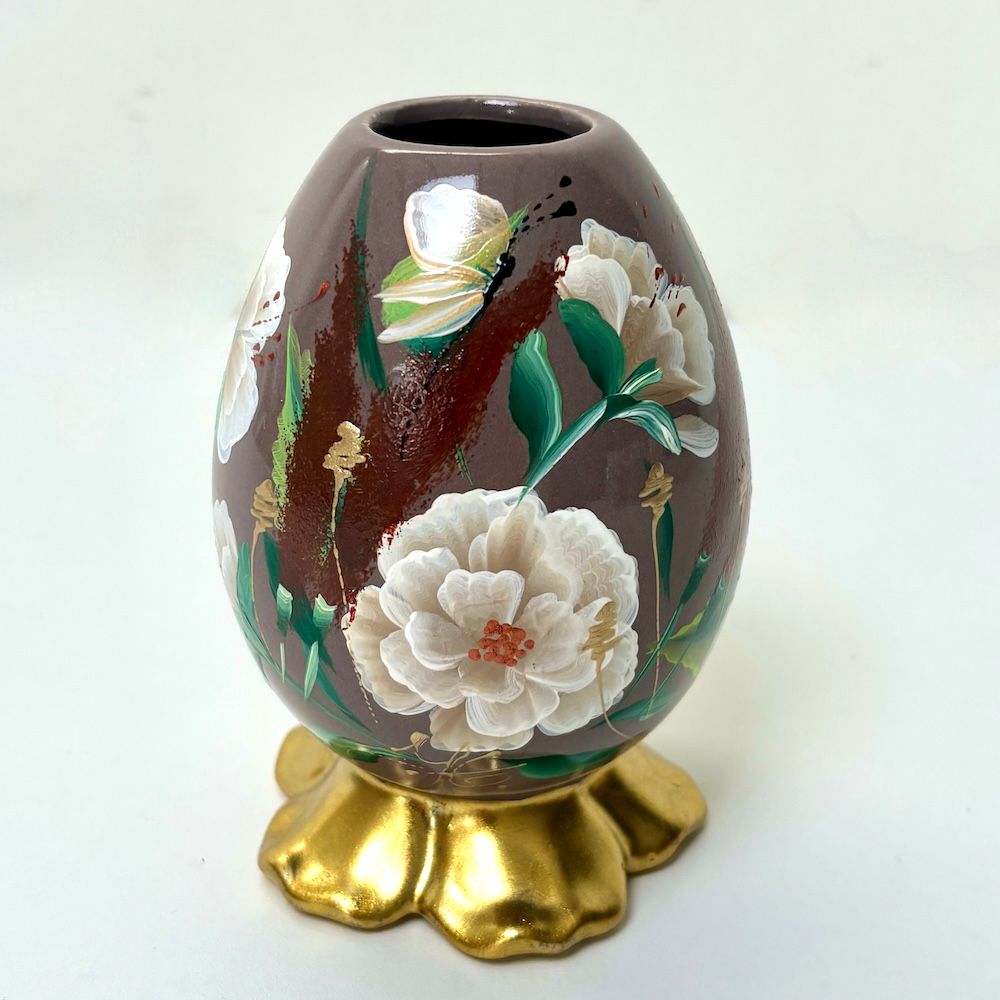 Een stoffig roze porseleinen eivormige vaas met handgeschilderde witte bloemen en rode accenten, rustend op een  gouden voet.
