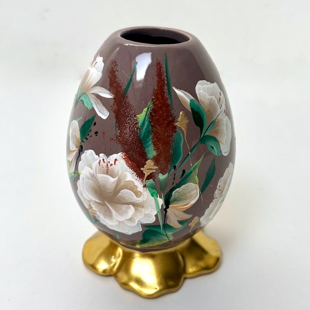 Een stoffig roze porseleinen eivormige vaas met handgeschilderde witte bloemen en rode accenten, rustend op een  gouden voet.